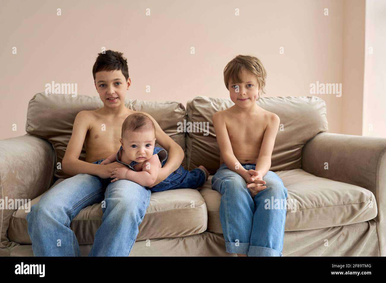 Two dark-skinned brothers posing on a white background in casual clothes.  The little boy with