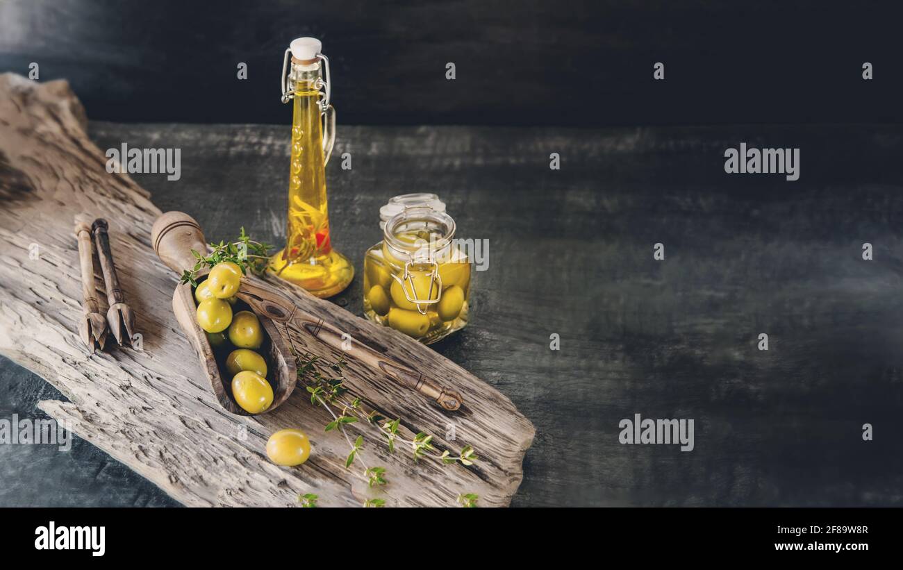 Green olives in a glass jar on a wooden background, a bottle of olive ...