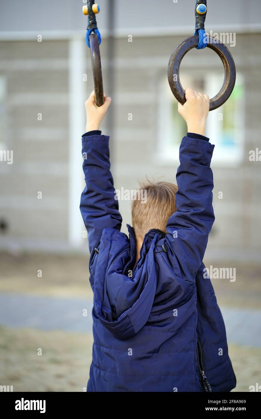 Kids Using Playground Rings Little child swings on sports rings in yard of house. Active boy ...
