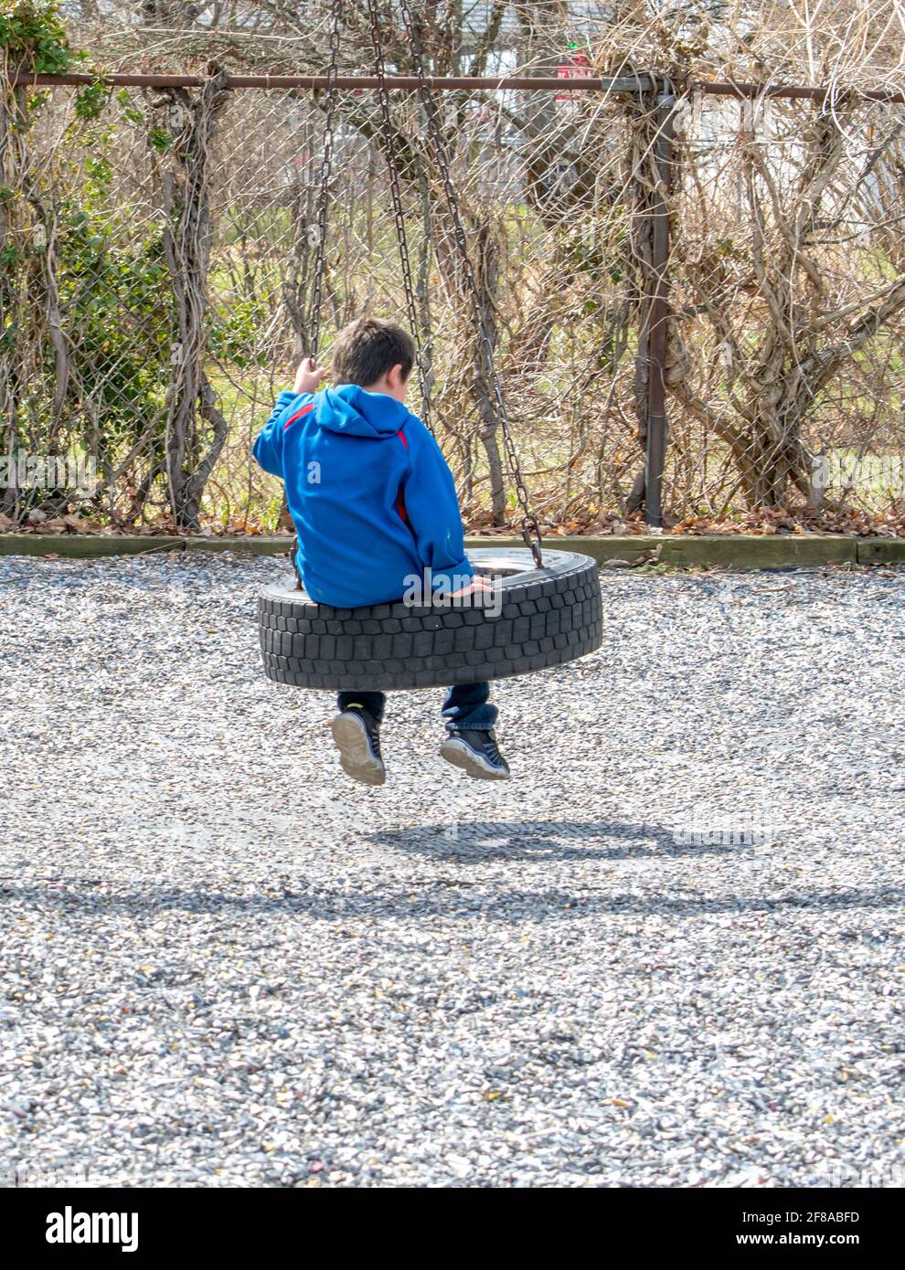 lonely child sits by himself on a tire swing Stock Photo