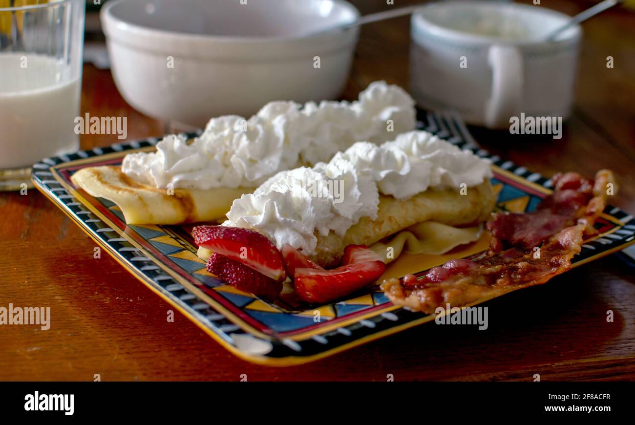 delicious strawberry crepes are topped with sweet whipped cream and served with bacon Stock Photo