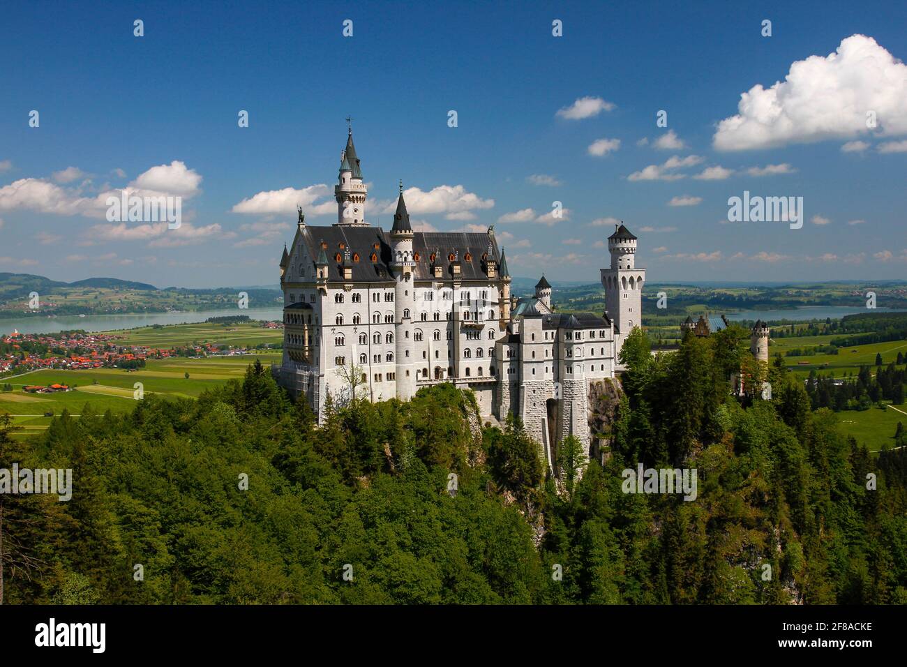 Fairytale Neuschwanstein Castle Perched on Green Mountain with Bright Blue Sky, Bavaria, Germany Stock Photo