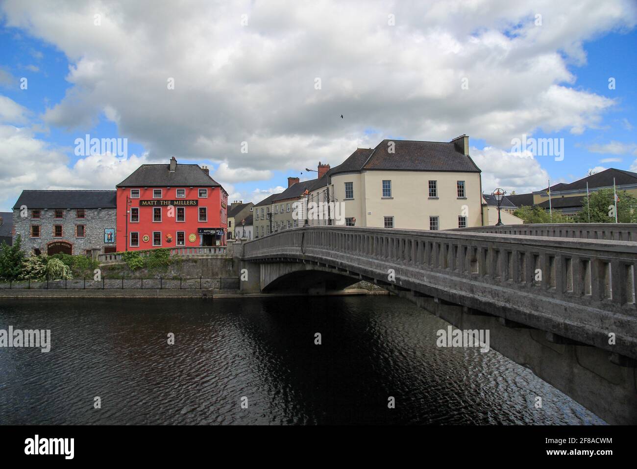 Stone bridge over water leading to colorful buildings with blue sky in Ireland Stock Photo