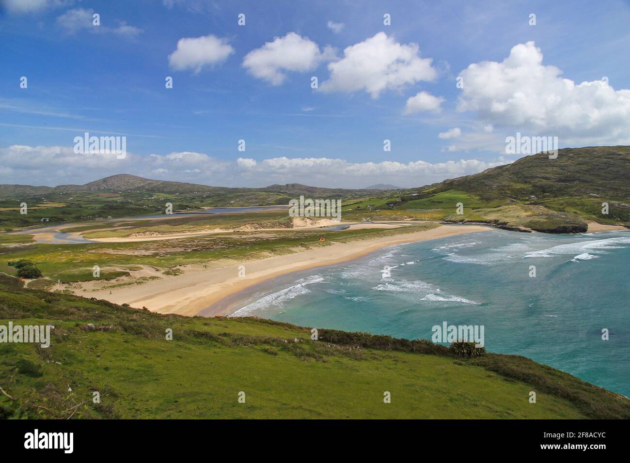 Beautiful Rolling Green Hills of Ireland Against a Blue Sky and Clear Blue Green Water with Sand along Coast, Ireland Stock Photo