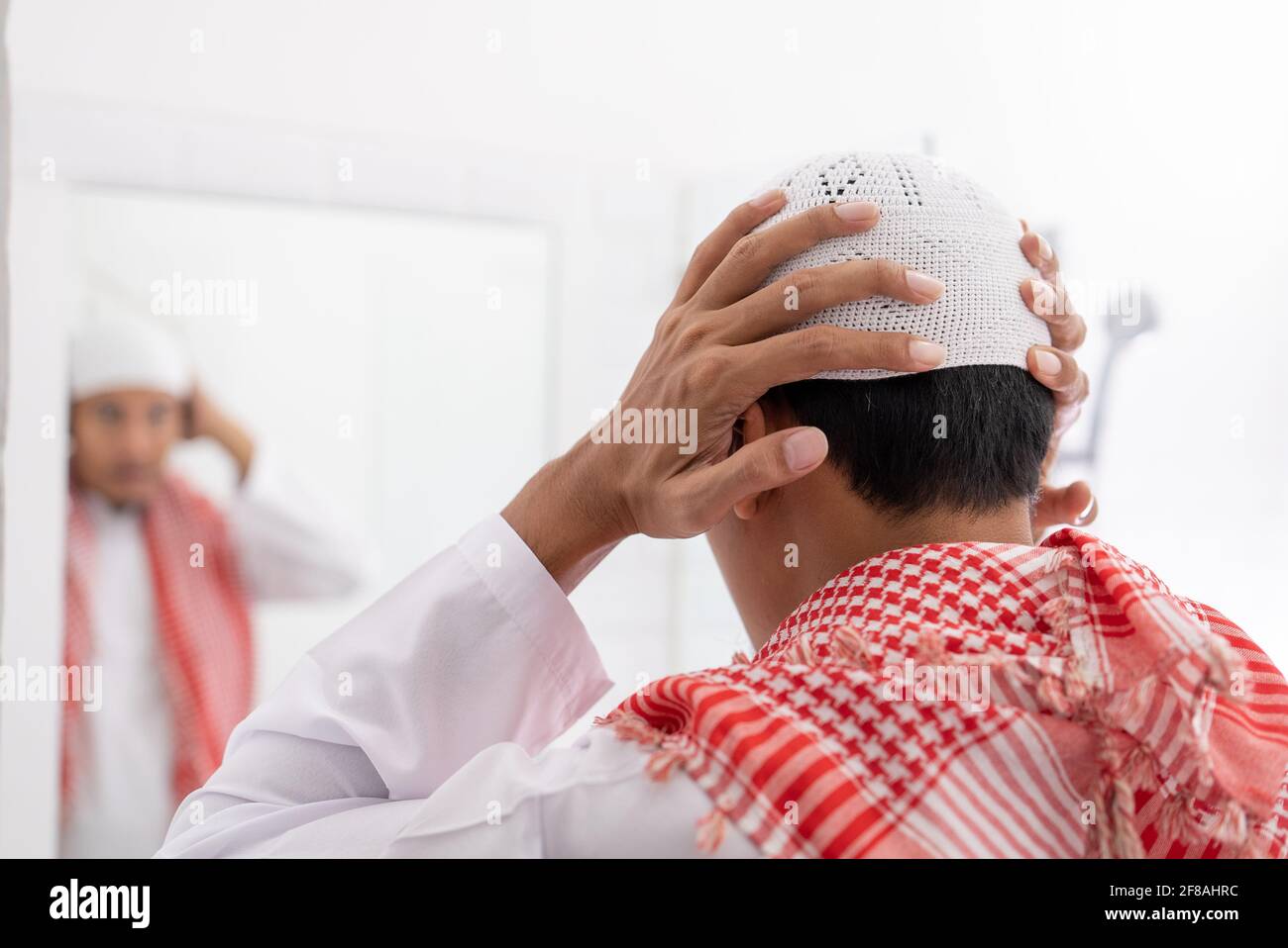 muslim man looking at mirror and get dressed wearing islamic hat or cap