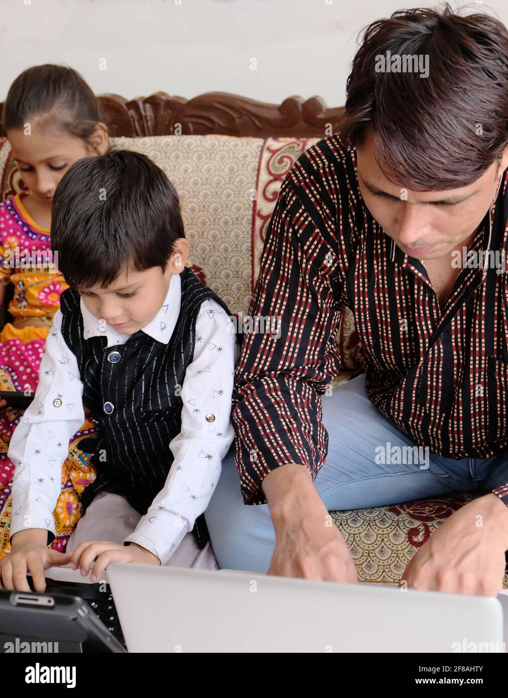 Indian family using various technologies while sitting on sofa at home Stock Photo