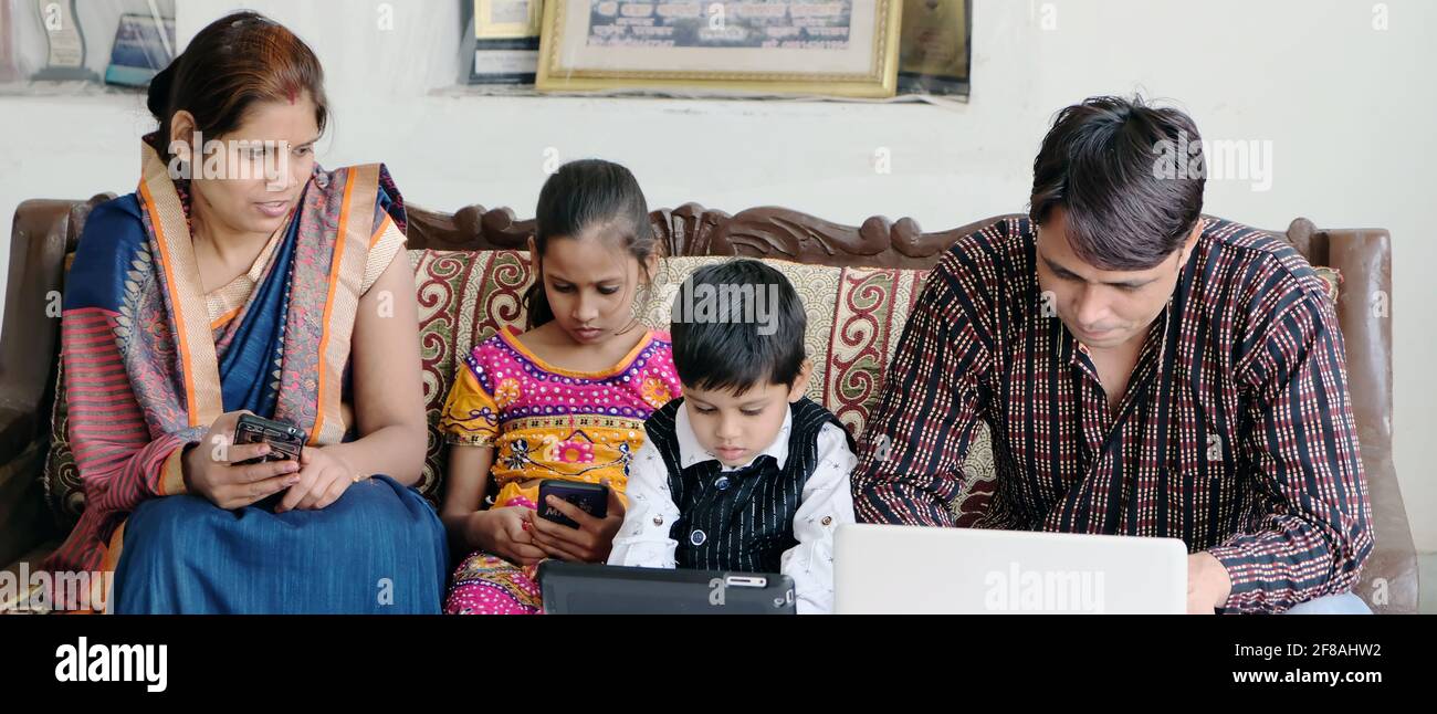 Indian family using various technologies while sitting on sofa at home Stock Photo