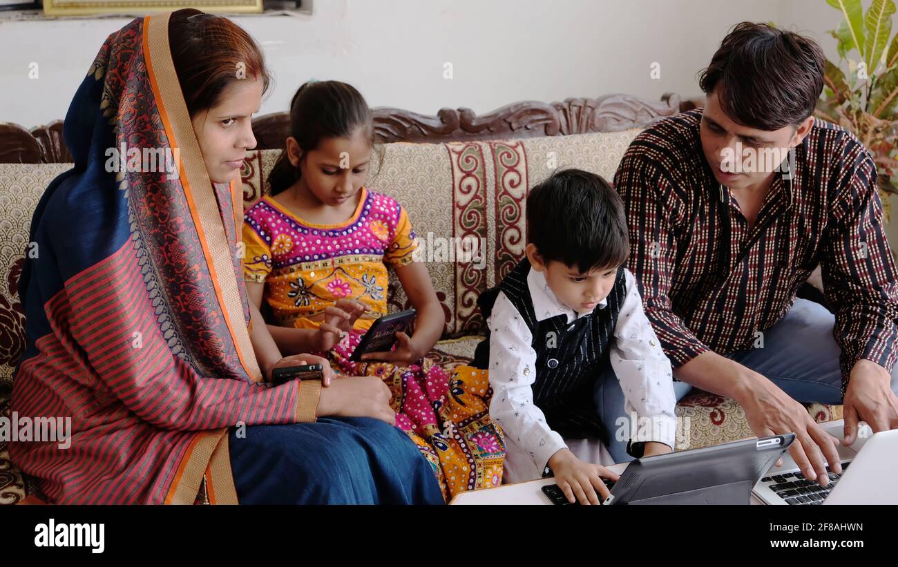 Indian family using various technologies while sitting on the sofa at home Stock Photo