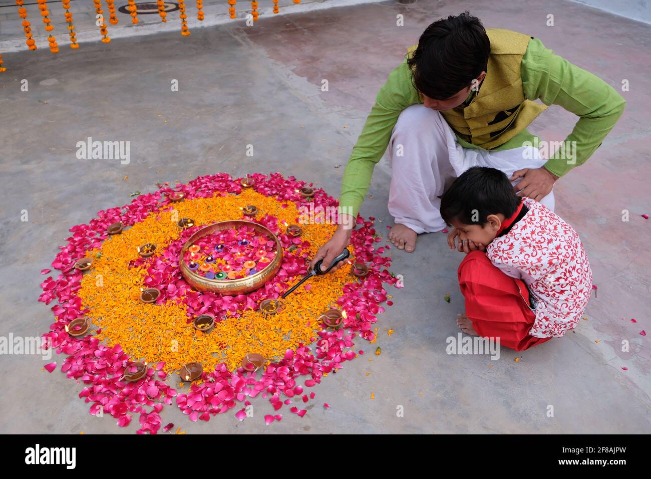 Indian male with his son creating rangoli using candles, marigold and ...
