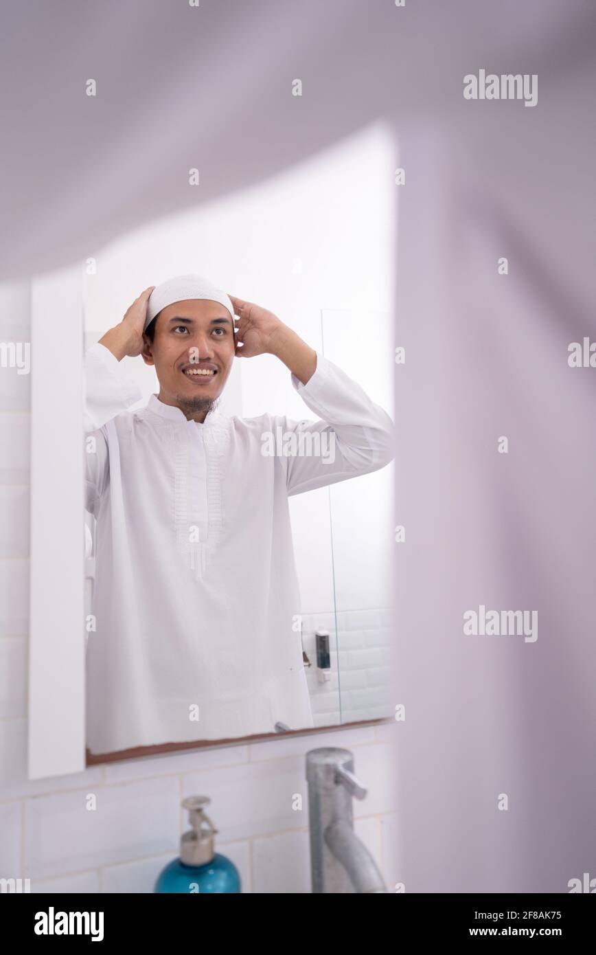 muslim man looking at mirror and get dressed wearing islamic hat or cap