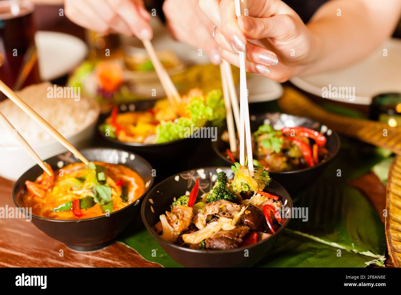 Young people eating in a Thai restaurant, they eating with chopsticks, close-up on hands and food Stock Photo