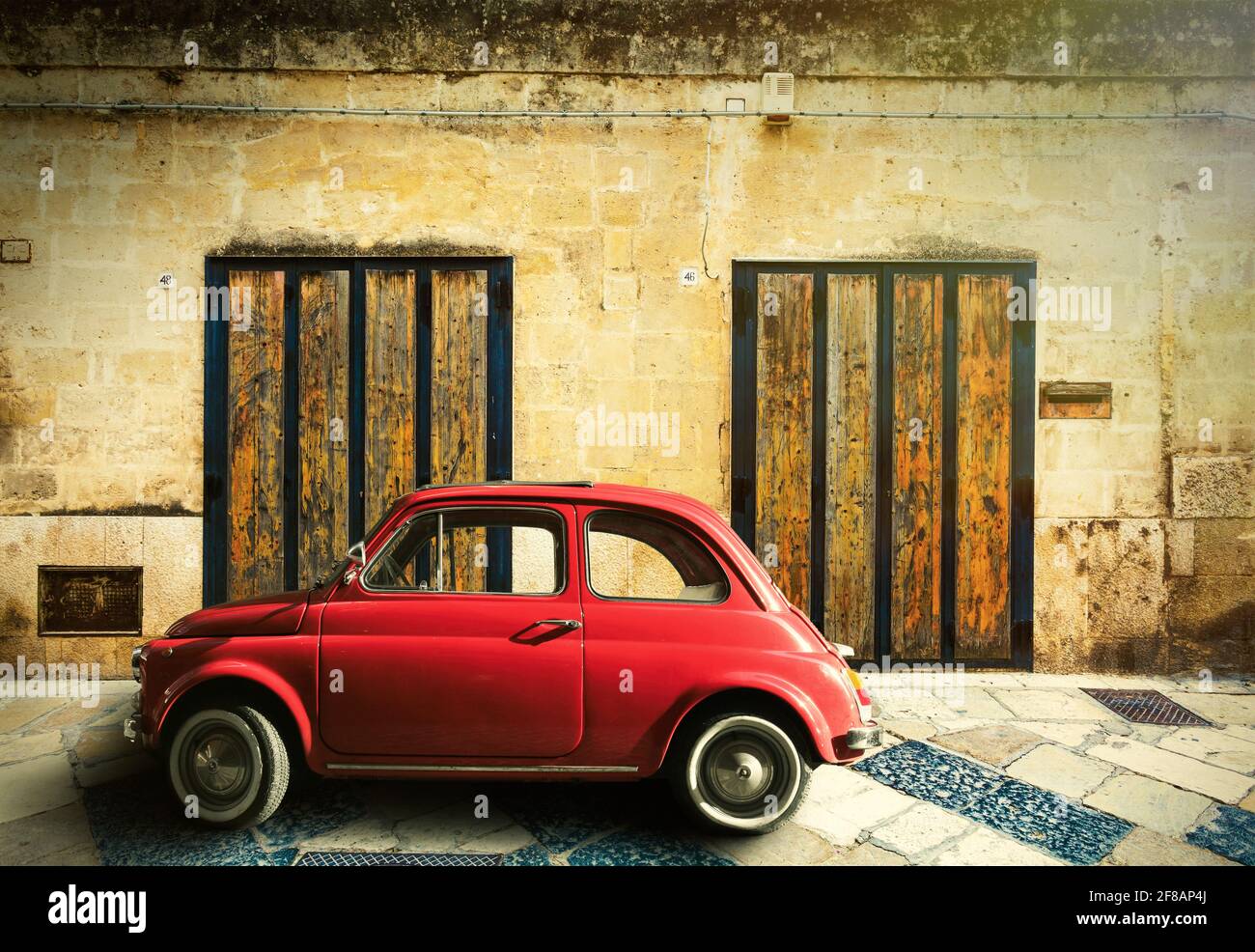 Beautiful scene of a small red Italian vintage car. Ancient house with two wooden doors. Location: Matera, Italy Stock Photo