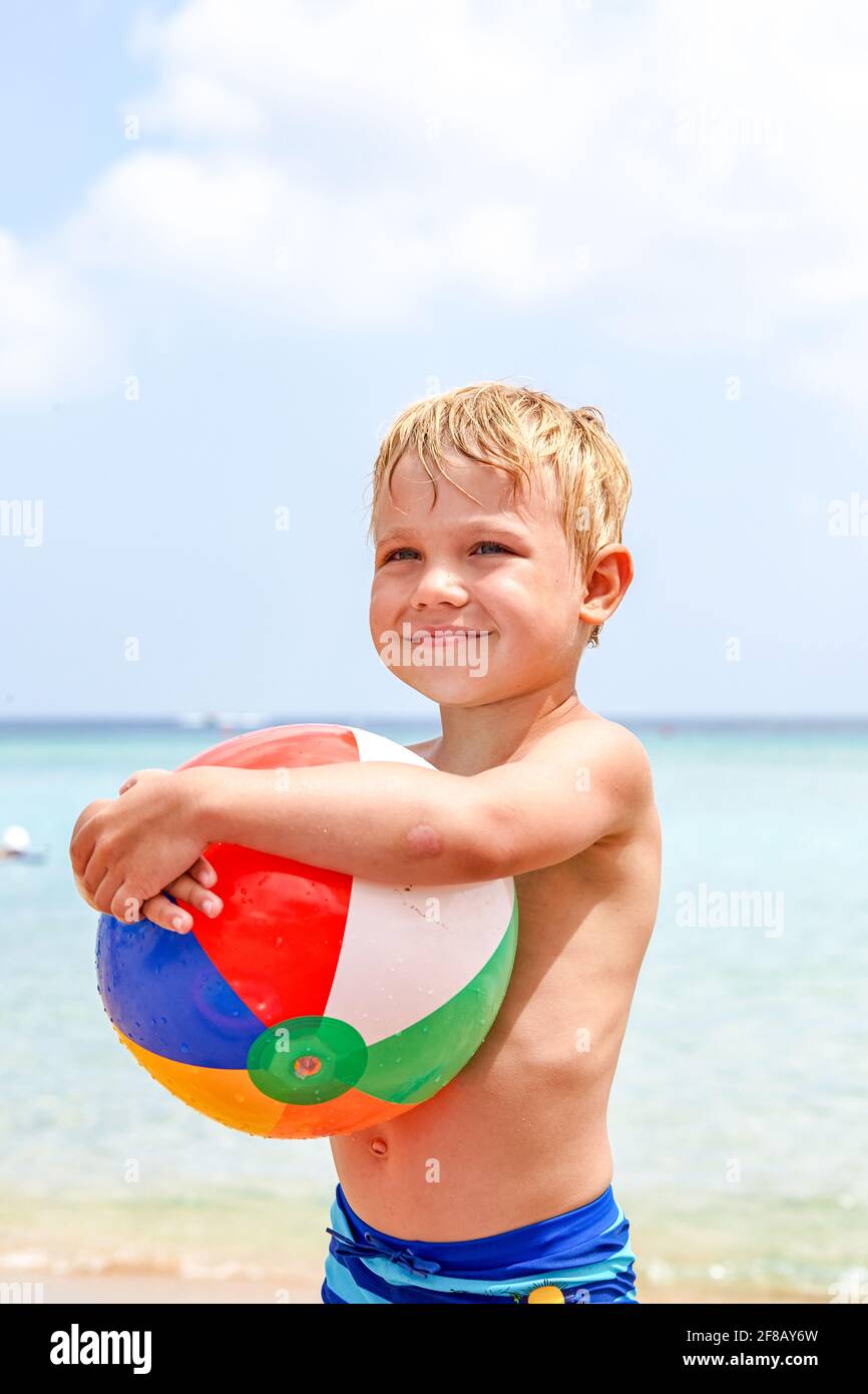excited laughing boy holding colorful beach ball at the beach enjoying
