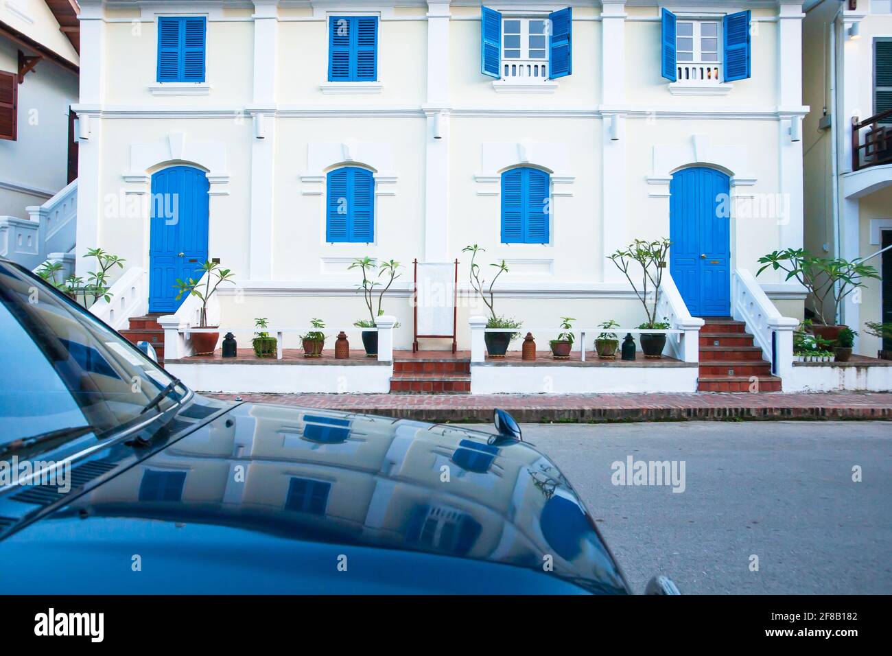 Picturesque colonial buildings on the street in Luang Prabang, Laos, vintage blue doors and windows of colonial building reflects on a blue car. Stock Photo