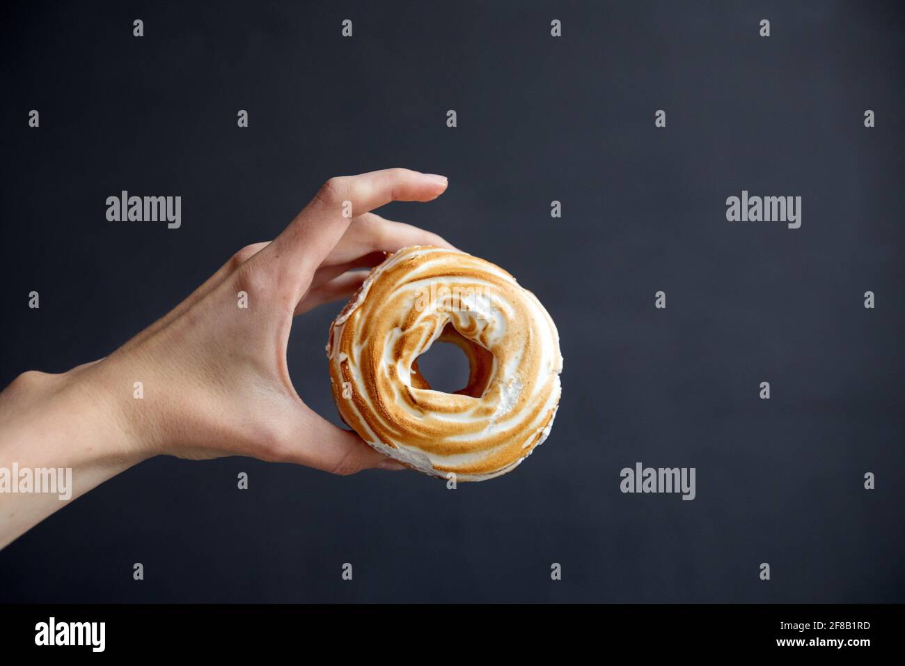 Unrecognizable person demonstrating delicious sweet French cruller near empty space against black background Stock Photo
