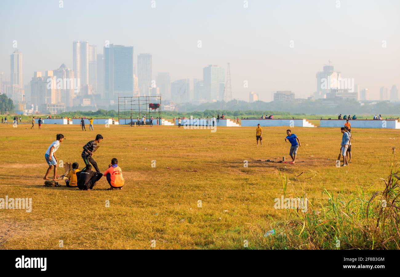 MUMBAI, INDIA - December 29, 2021: Kids playing cricket in a park in Mumbai with skyscrapers in the background Stock Photo