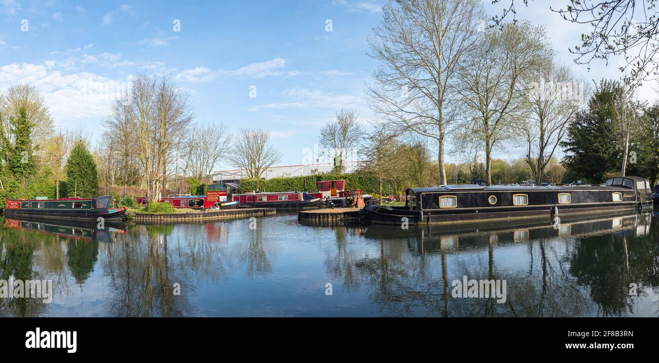 Canal boats moored on the Kennet and Avon Canal at the entrance of Newbury Boat Company with trees and reflections, no people. Newbury, Berkshire. Stock Photo