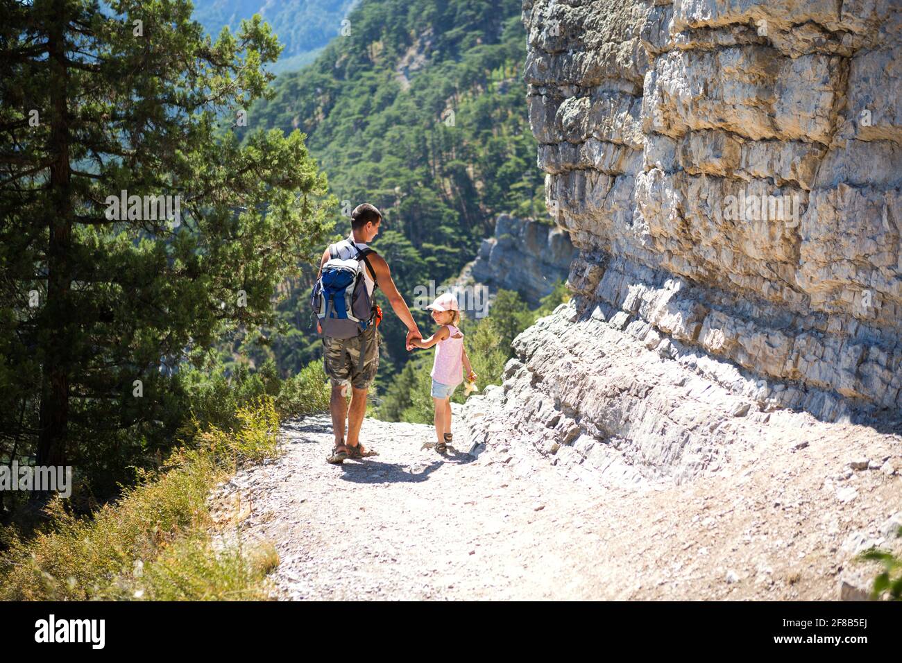 Dad and daughter go hiking on a mountain trail. Active family holidays, healthy lifestyle, trekking with a backpack, adventures of a young tourist. Stock Photo