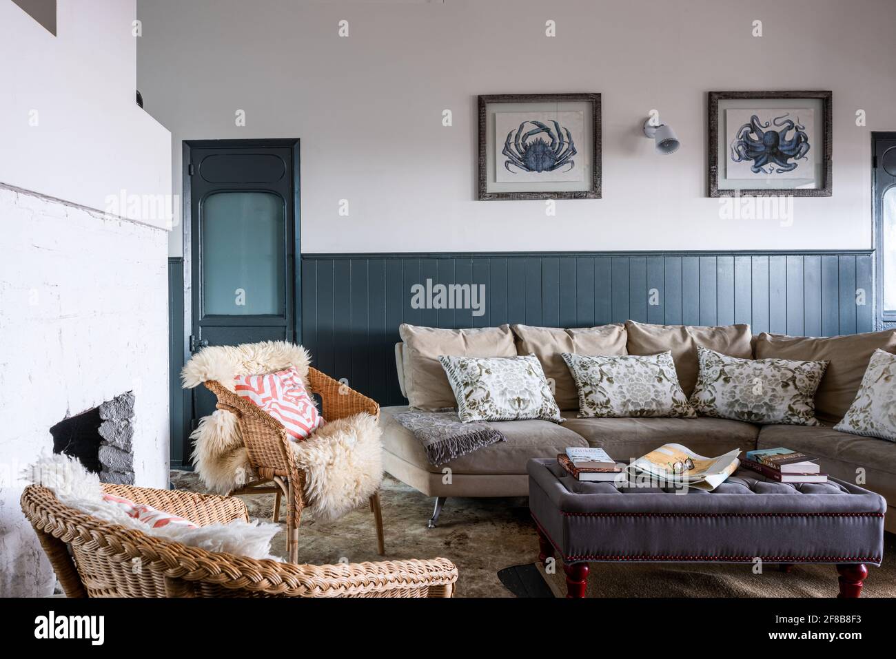 Sofa with cushions from Designers Guild and wicker chairs with sheepskin throws with  paintwork in Downpipe in renovated West Sussex holiday home. Stock Photo