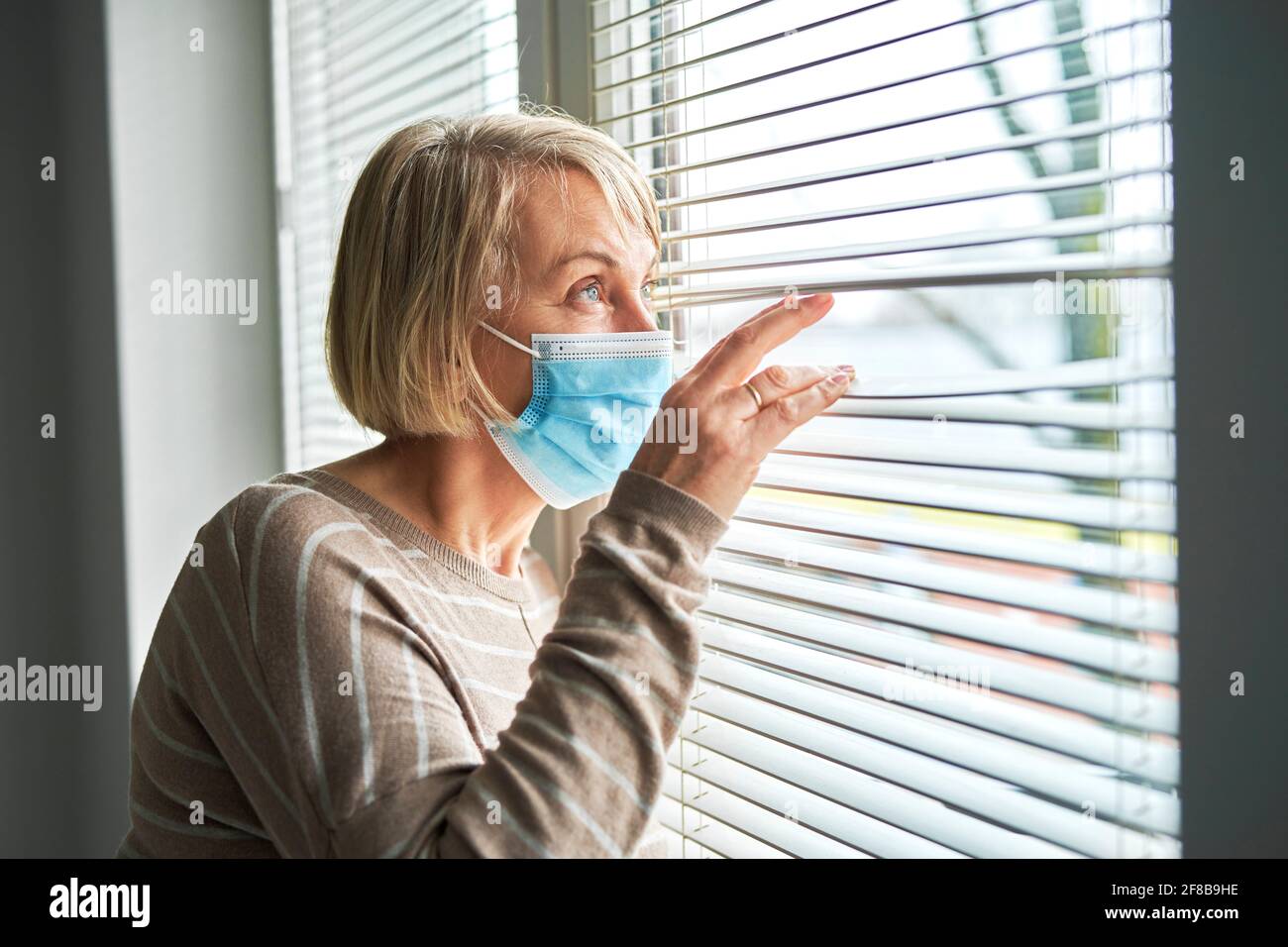 Senior woman in protective mask looking out the window at home Stock Photo