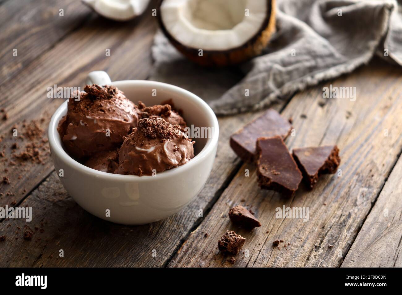 Chocolate coconut vegan ice cream in a white cup. Ice cream balls with chocolate. Wooden background, copy space. Stock Photo