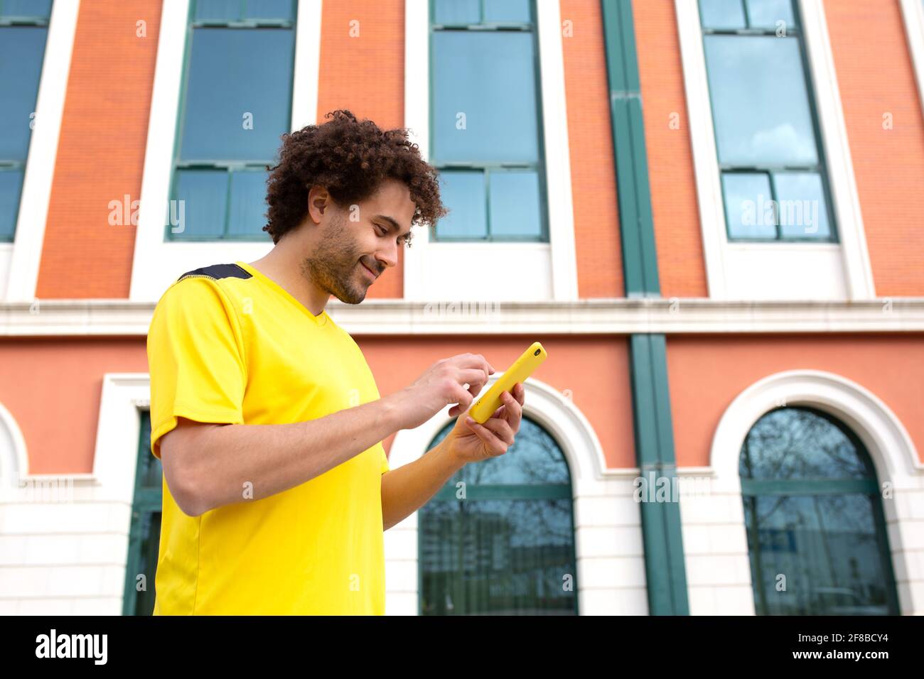young latino male athlete in yellow t-shirt looks at his cell phone after a workout Stock Photo