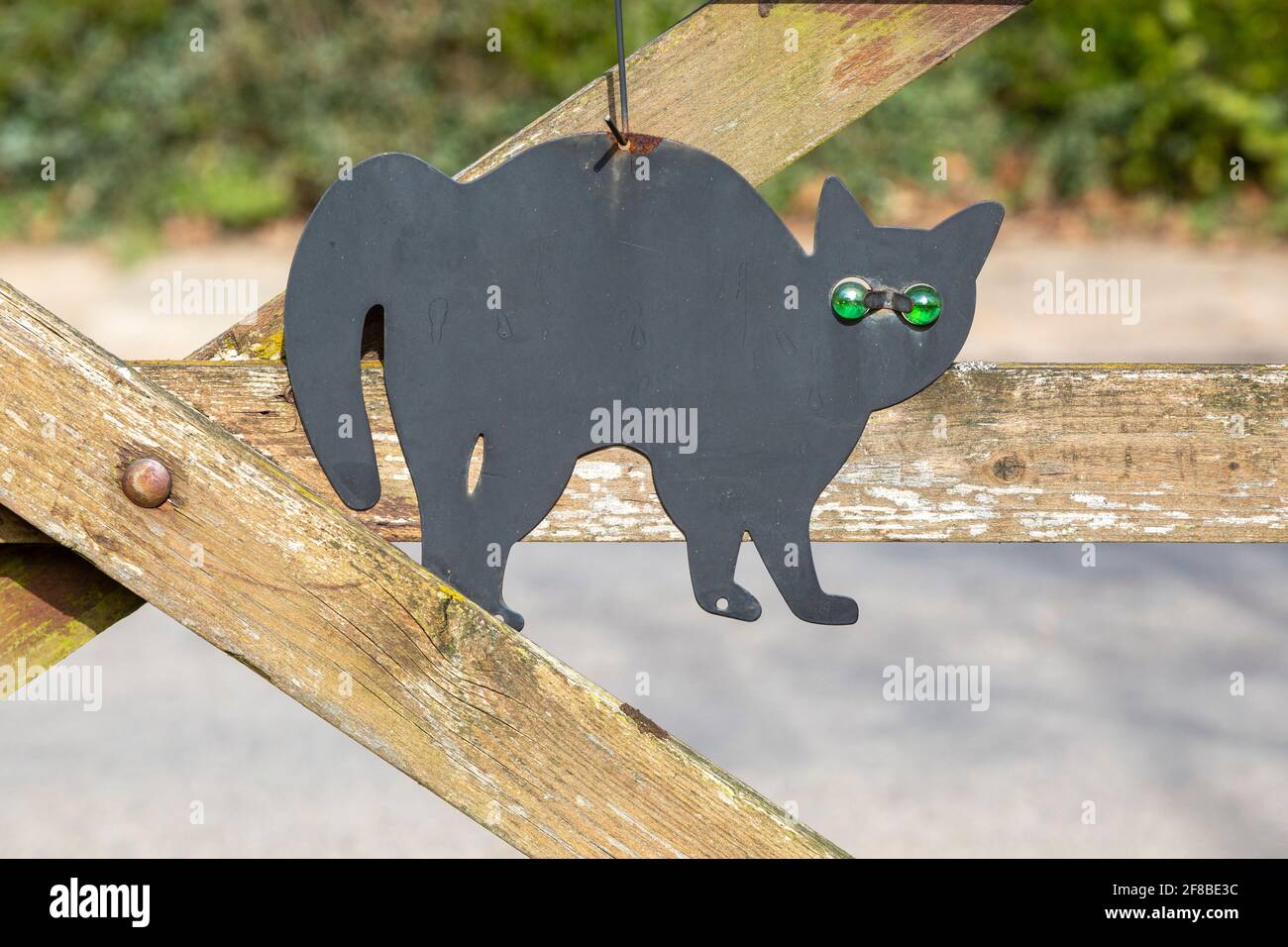 Black metal cat scarer with green glass eyes hanging from wooden gate