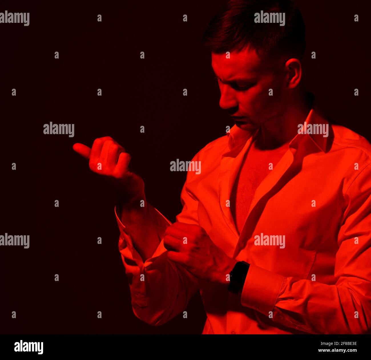 Portrait of young businessman in official wear taking off unbuttoning his shirt. Red light filter, gel Stock Photo