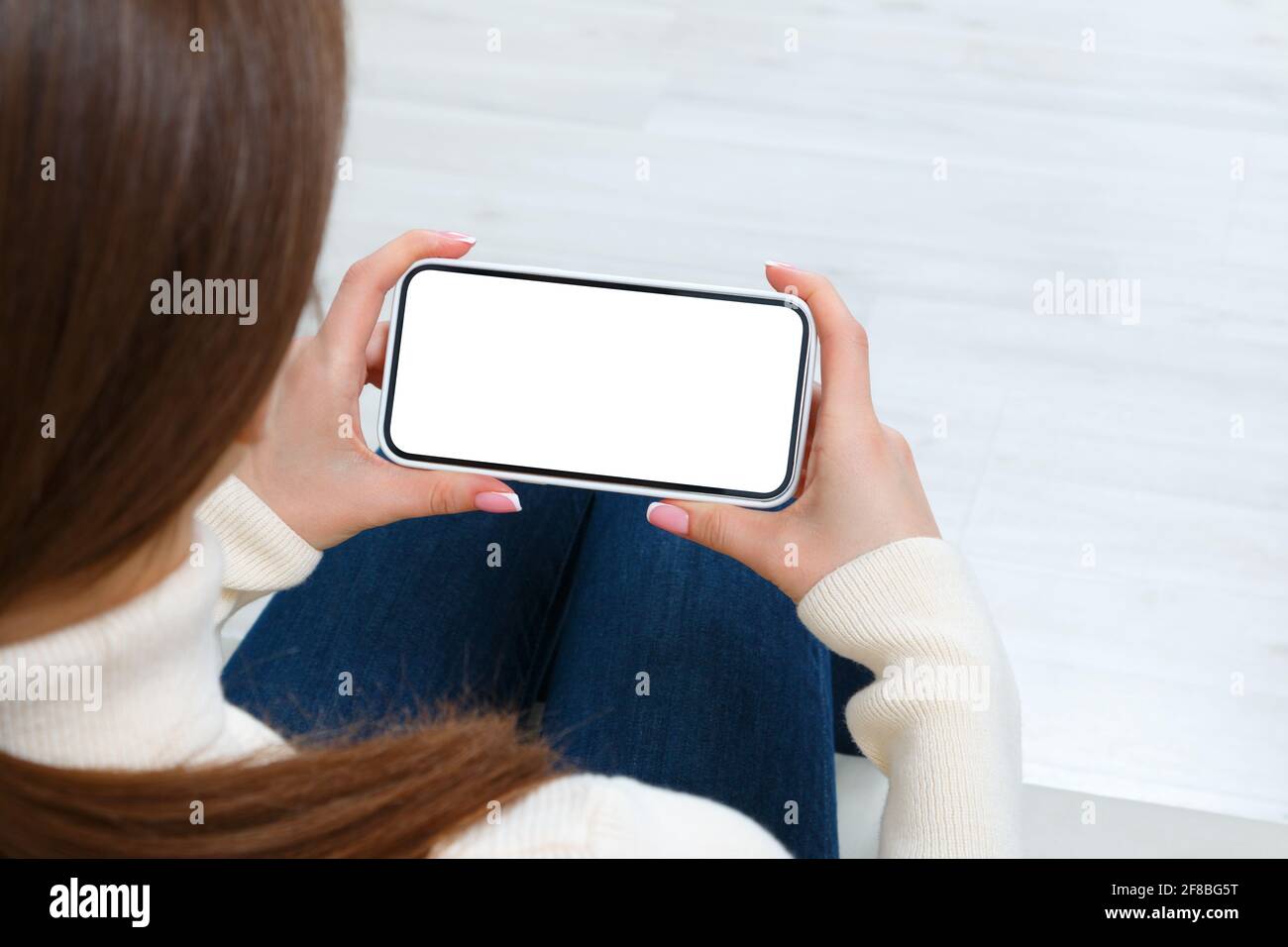 Rear view of girl using phone with white blank screen mockup. Lifestyle concept with digital technology. Stock Photo