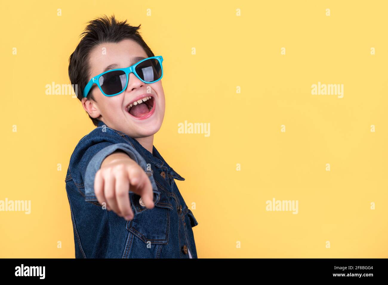 happy and smiling kid with sunglasses pointing with the finger and copy space on a yellow background Stock Photo