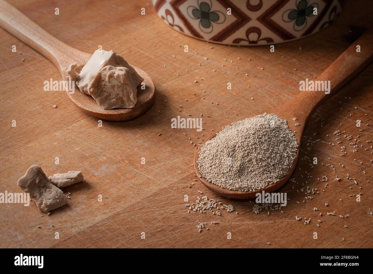 Fresh yeast and instant dry yeast on wooden spoon on a wood cutting board Stock Photo