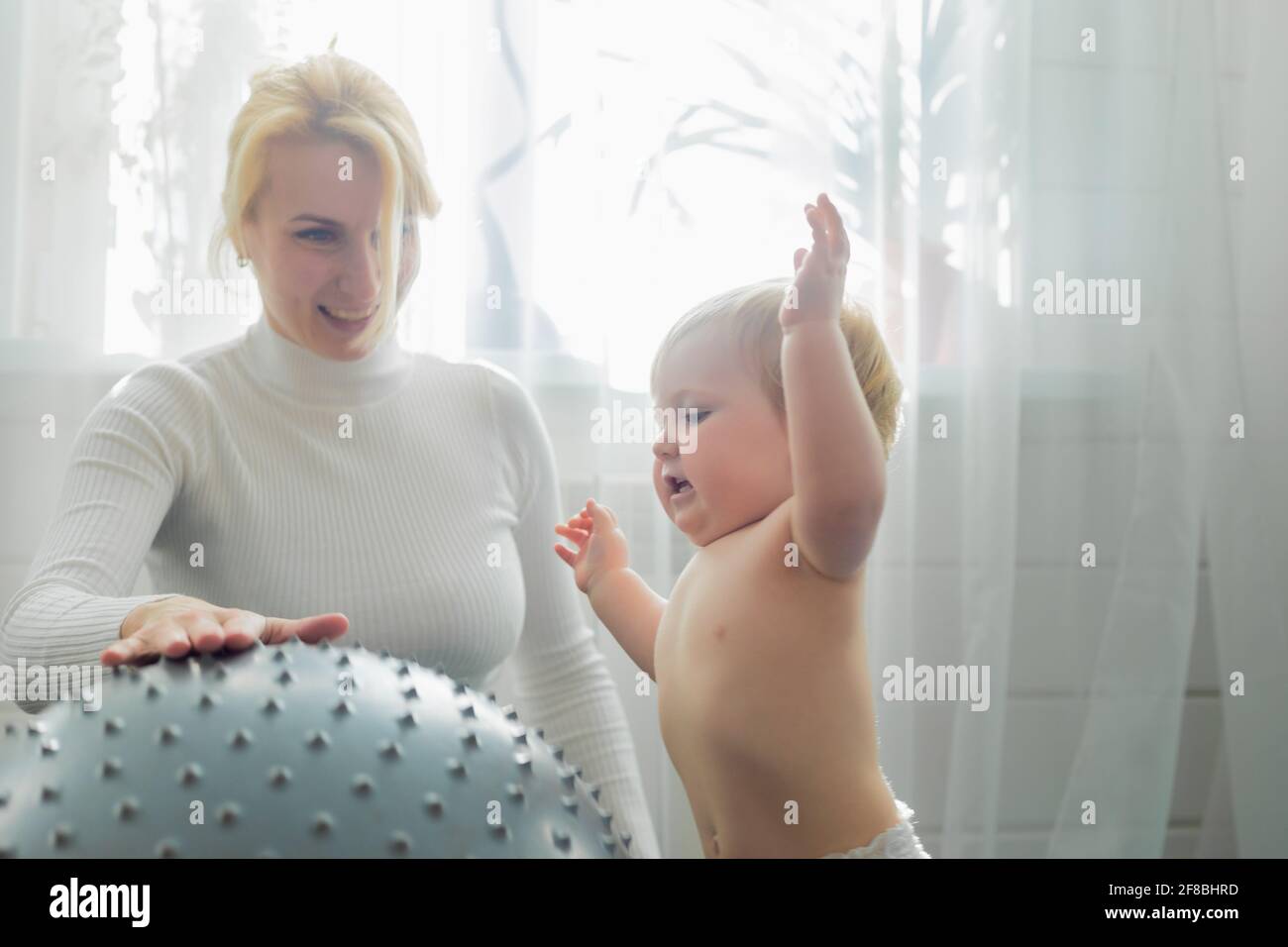 Mom is engaged in gymnastics with the baby on an inflatable ball. Fitball, gymnastics for a child. Stock Photo