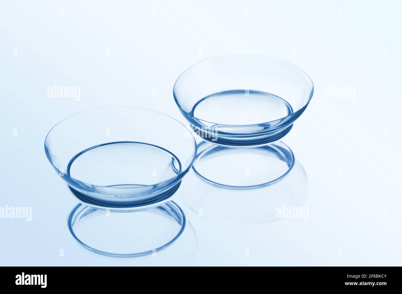 Two contact lenses with reflections on a blue background. Focus on long-distance lens. Stock Photo