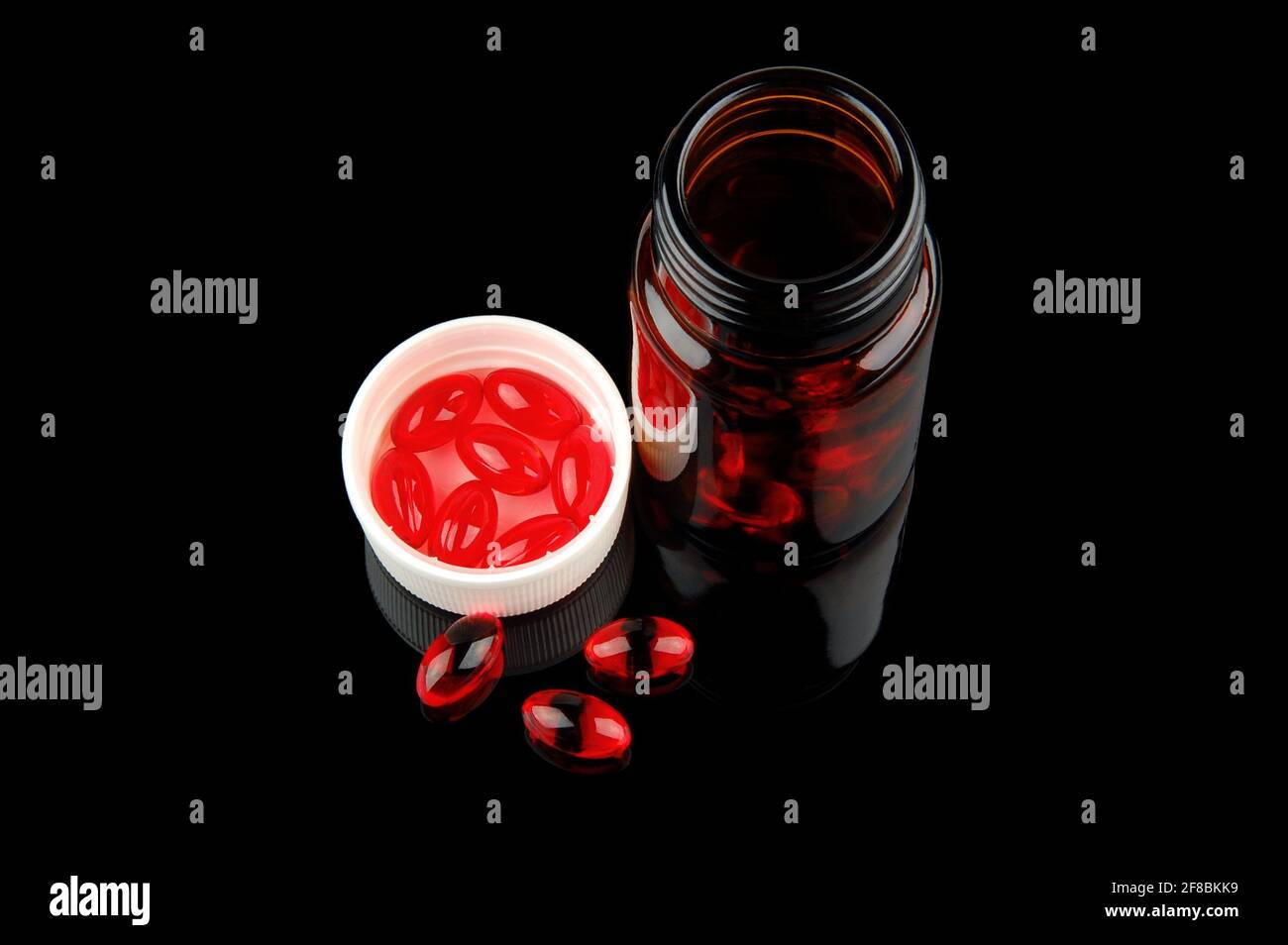Red vitamin pills in vial on glossy black background Stock Photo