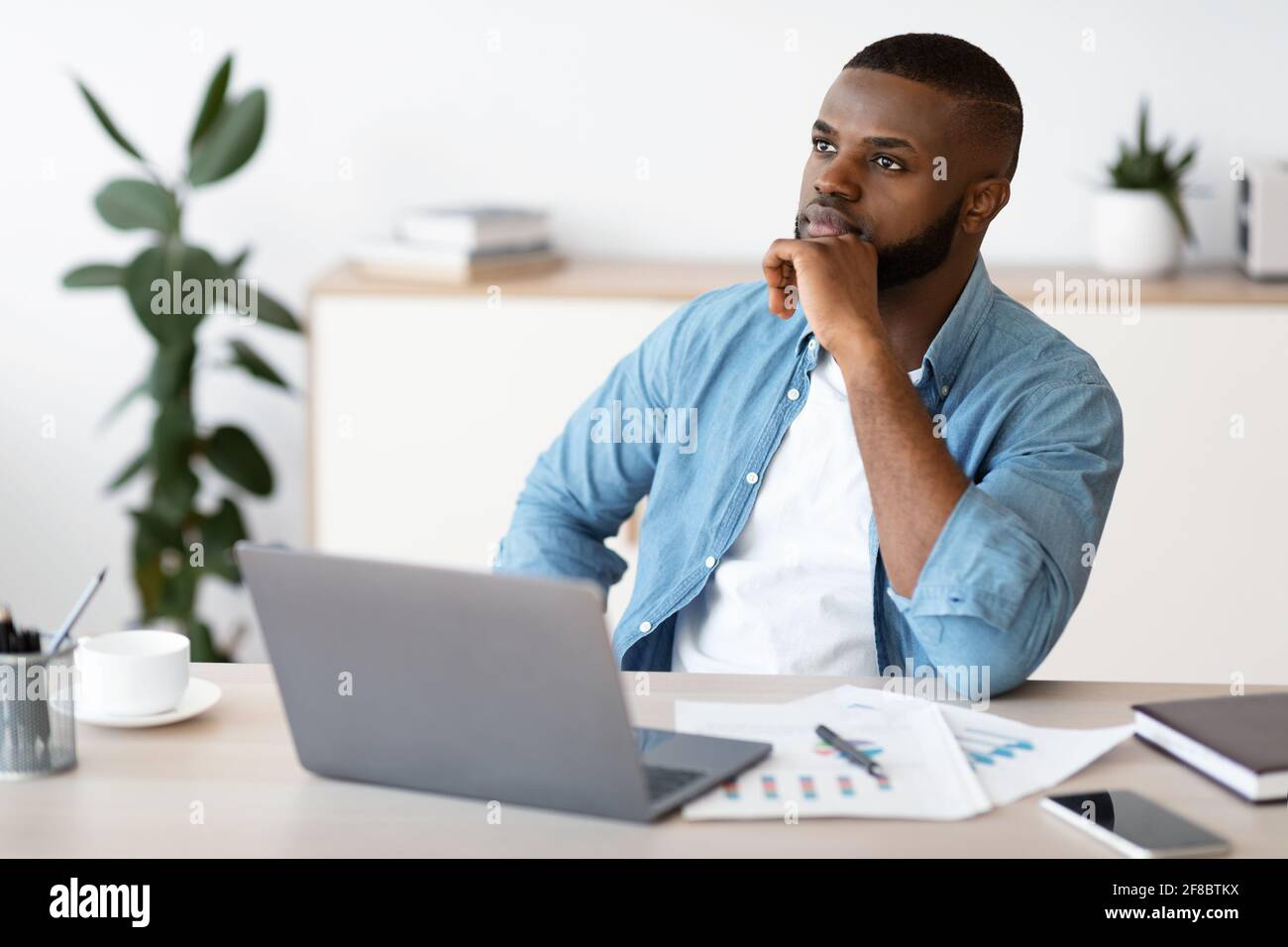 Black Freelancer Guy Sitting At Workplace With Thoughtful Face Expression Stock Photo