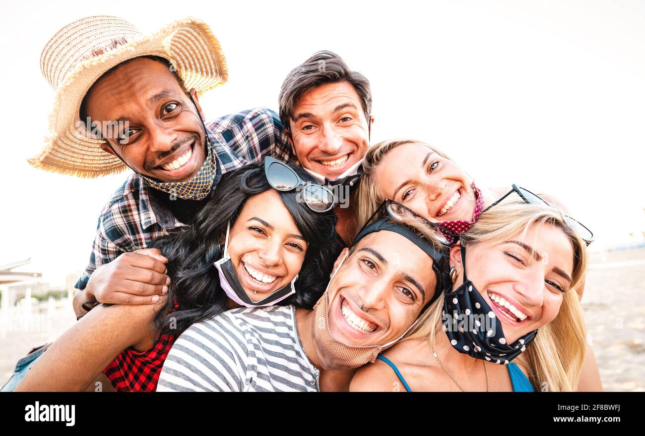 Multiracial friends taking selfie smiling over open face masks - New normal life style friendship concept with young people having fun together Stock Photo