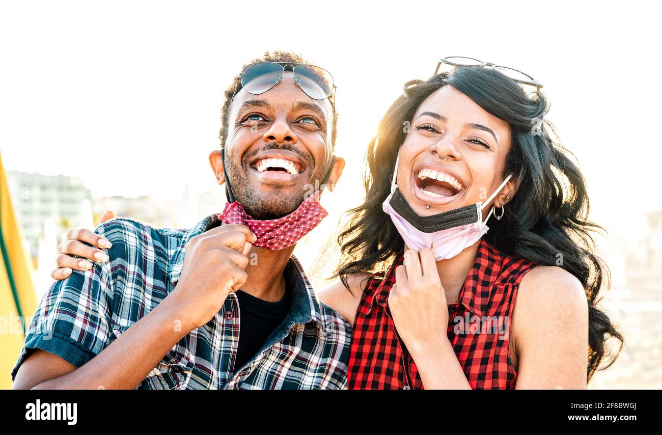 Young couple in love laughing over open face mask - New normal life style and relationship concept with happy lovers on positive mood at beach Stock Photo