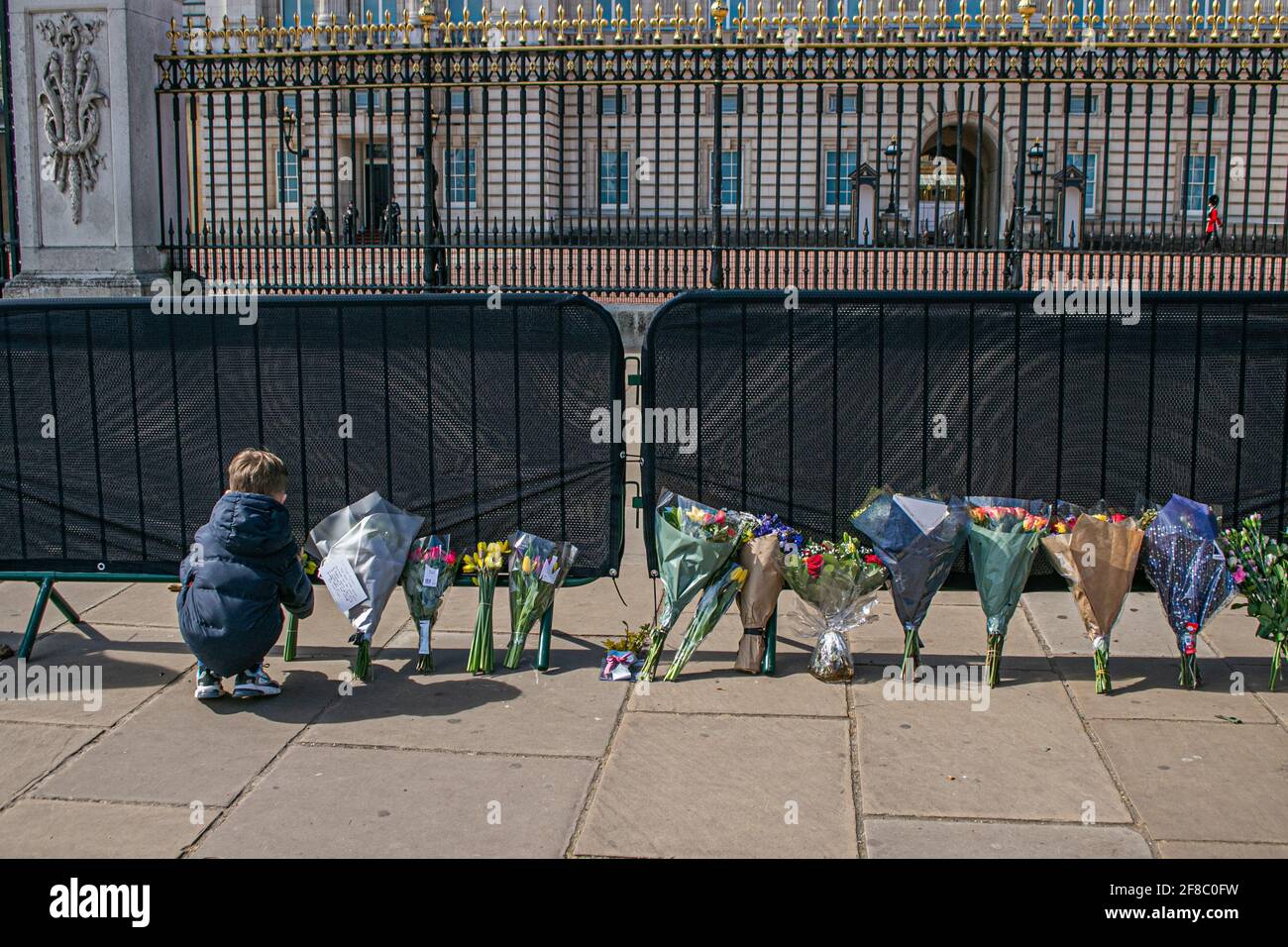 BUCKINGHAM PALACE LONDON, UK 13 April 2021. A young child leaves flowers and tributes outside Buckingham Palace in tribute to Prince Prince Philip, Duke Of Edinburgh despite being urged not to gather in large crowds and break COVID-19 restrictions. Her Majesty The Queen announced the death of her husband, His Royal Highness Prince Philip, Duke of Edinburgh aged 99 years who passed away peacefully April 9th and will be laid to rest on Saturday after a resticted cereminy on 17th April at Windsor Castle. Credit amer ghazzal/Alamy Live News Stock Photo