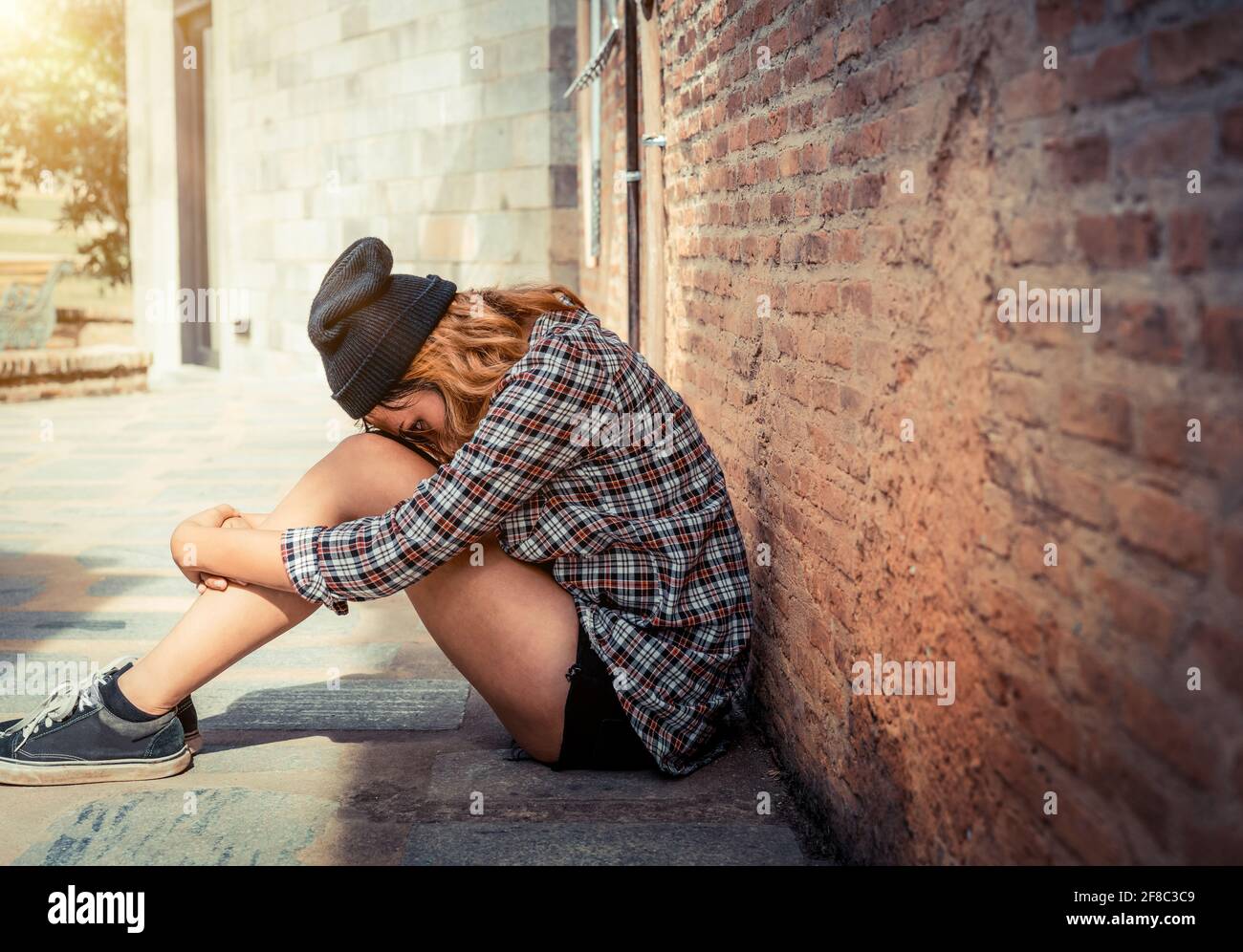 Depressed teenage woman feeling sad alone against brick wall in old town. Education and family failure concept. Stock Photo