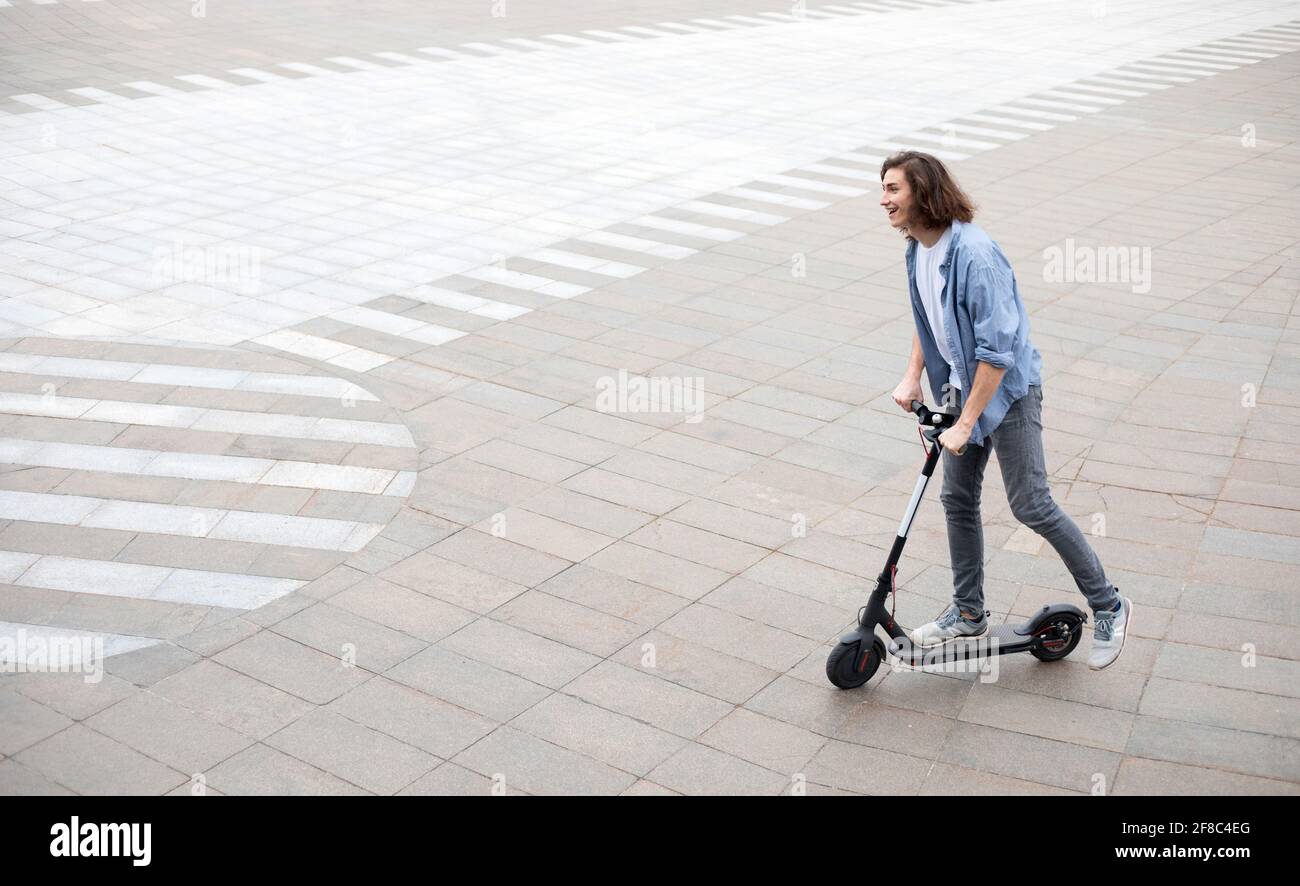 Excited guy having pleasant ride on electric kick scooter Stock Photo