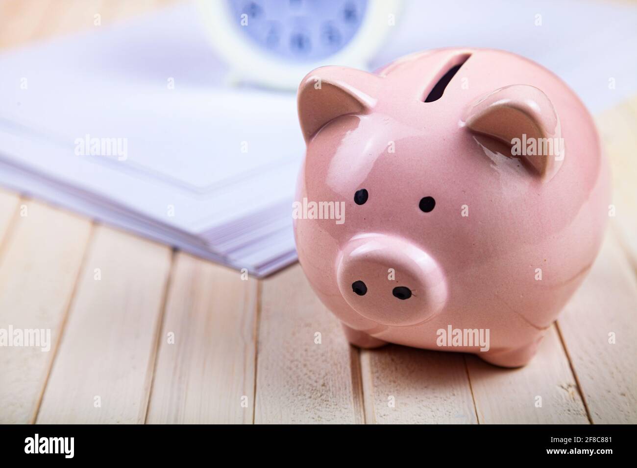 Pig piggy bank, paper and clock on a white wooden background. Time to save money. Stock Photo