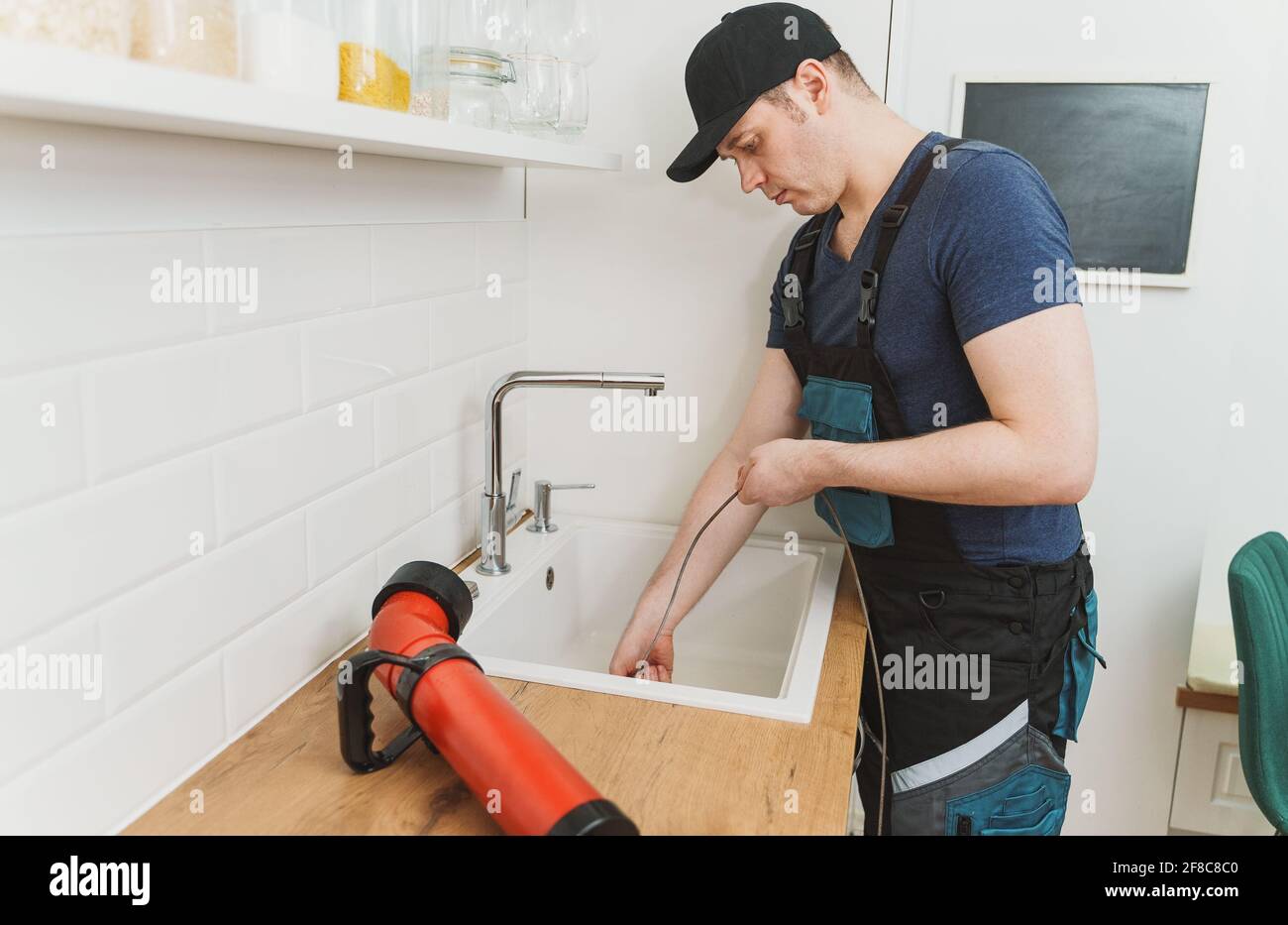 Plumber using drain snake to unclog kitchen sink. Stock Photo