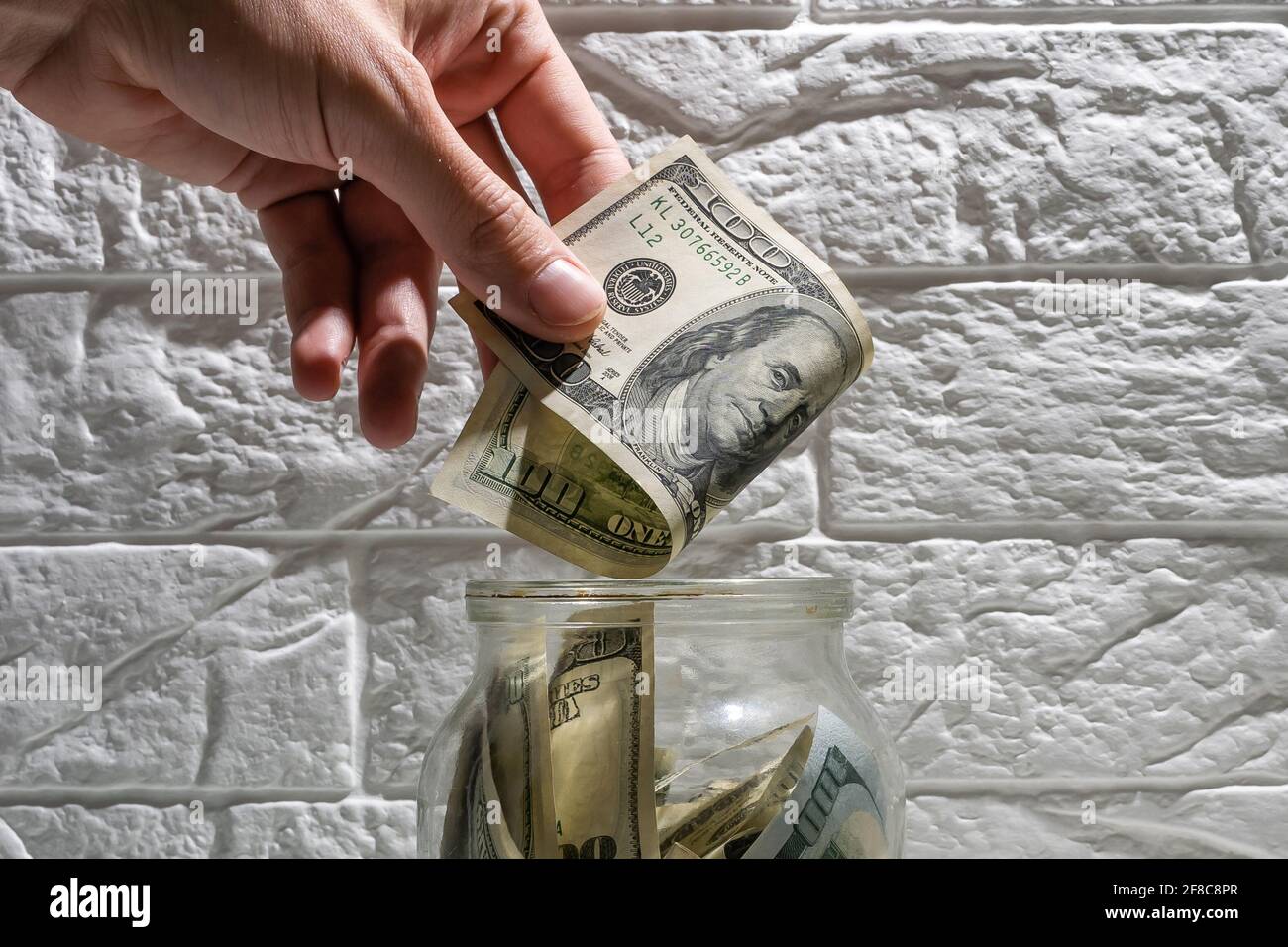 hand puts a bitcoin into the glass jar among real money background.  Accumulation of crypto currency, savings, investment, risk concept Stock  Photo - Alamy