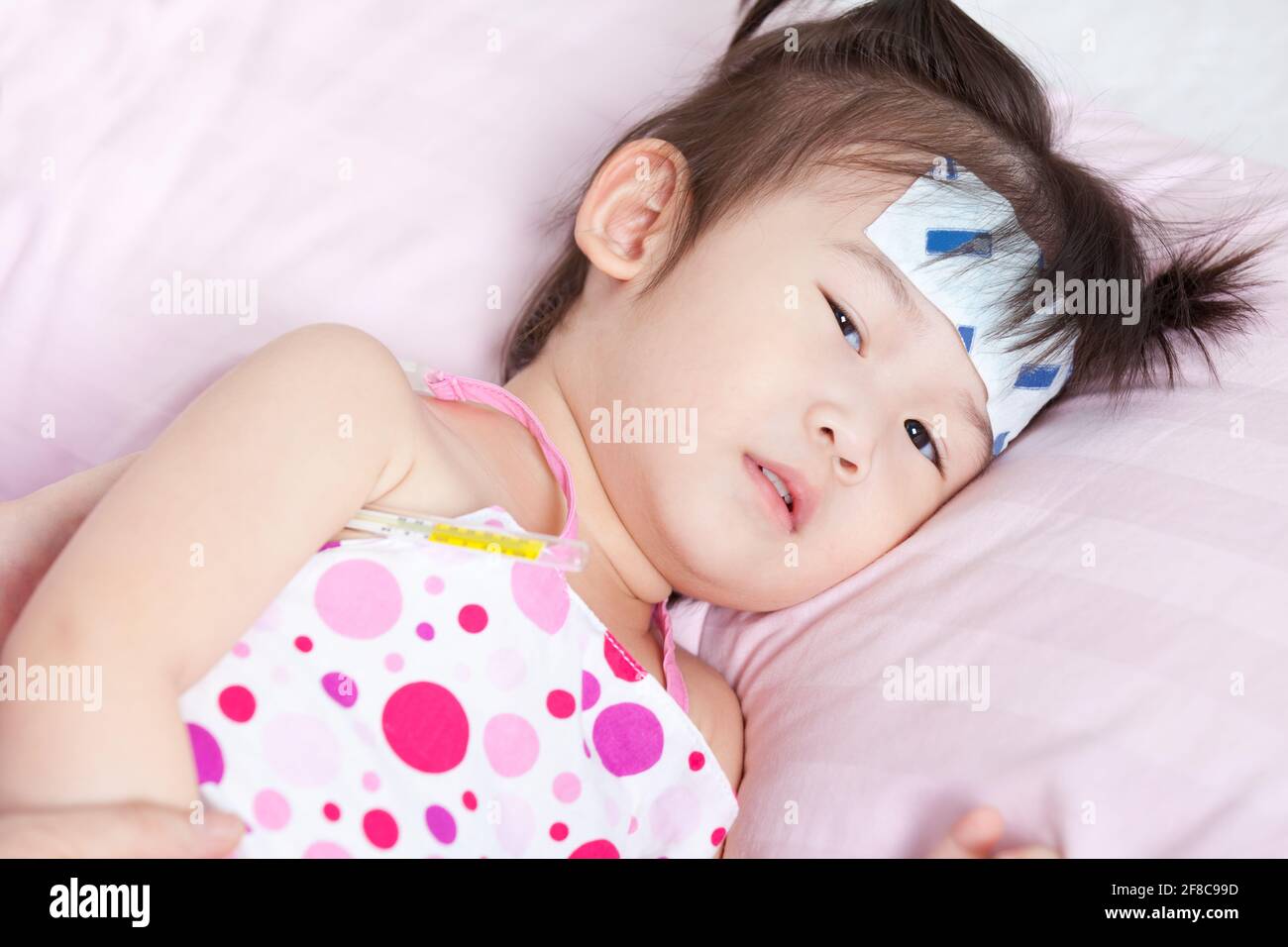 Closeup little asian girl lying on sickbed with mercury thermometer in