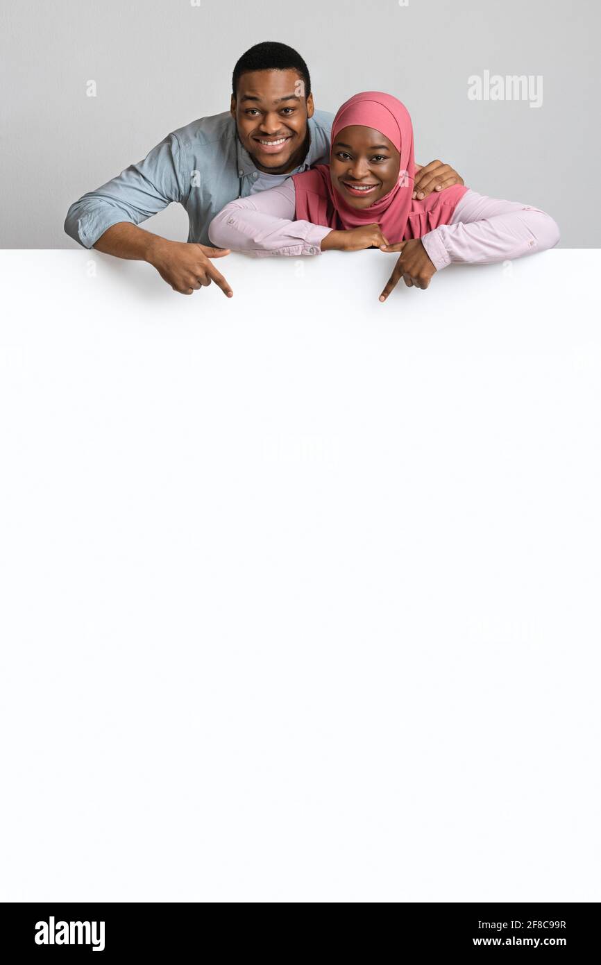 Happy loving black couple pointing at empty board Stock Photo - Alamy