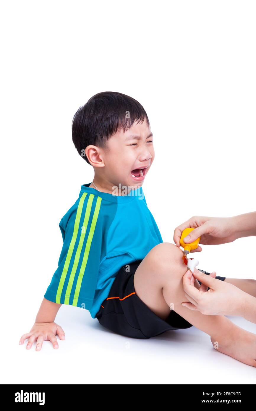 Portrait of a little asian boy (thai) crying, his mother provides first-aid at wound his leg, shoot in studio, Isolated on white background Stock Photo