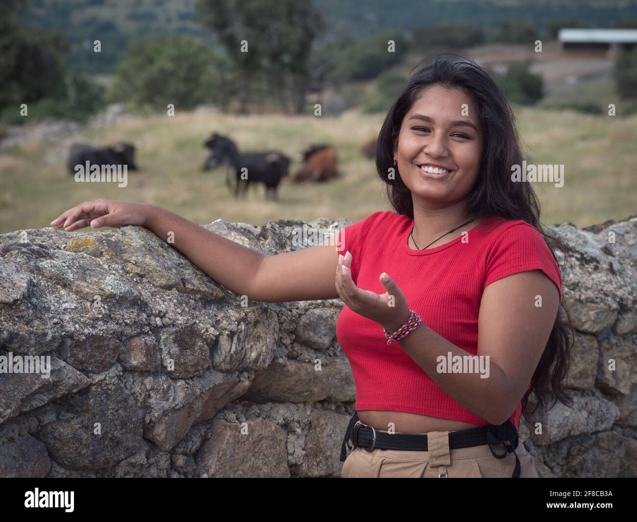 Optimistic asian female smiling at camera with herd of spanish bulls in the background. Stock Photo
