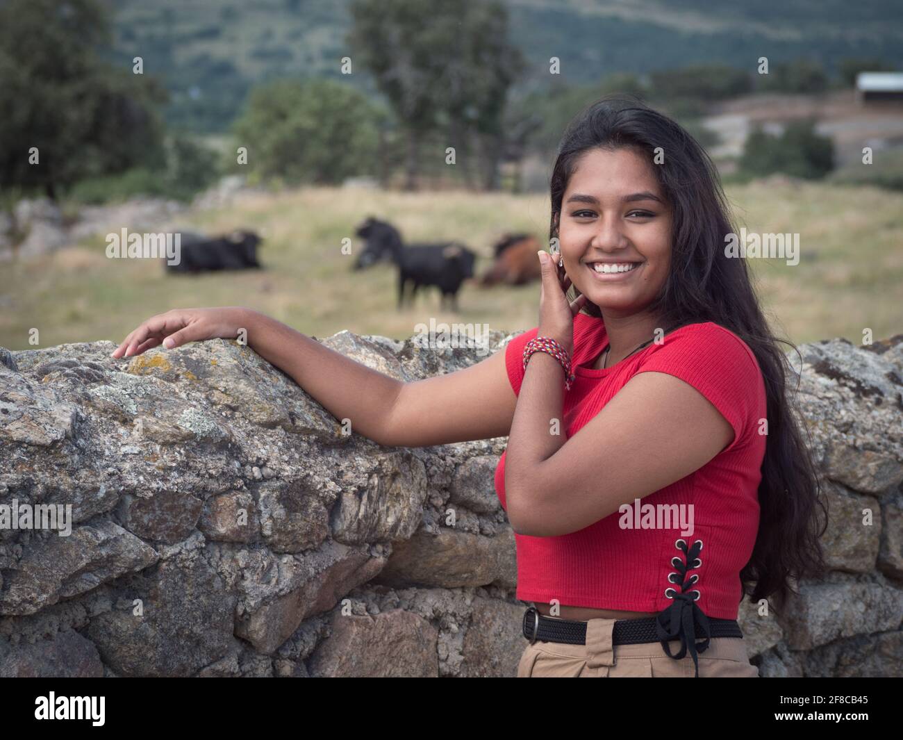 Confident asian female smiling at camera with herd of spanish bulls in the background. Stock Photo