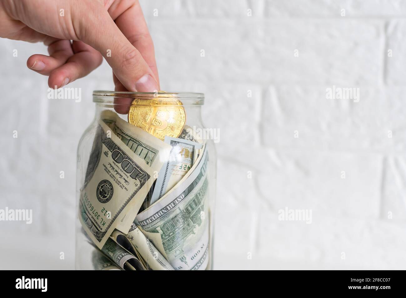 hand puts a bitcoin into the glass jar among real money background.  Accumulation of crypto currency, savings, investment, risk concept Stock  Photo - Alamy