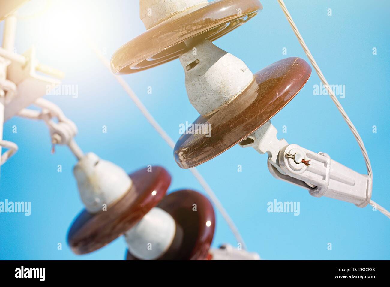 A ceramic suspended insulator hangs from a power line against a blue sky. Close-up. Stock Photo